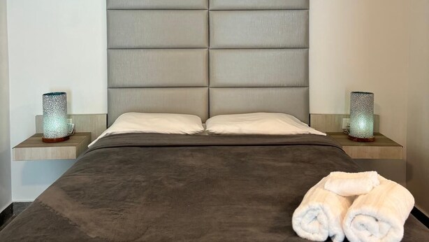 A modern hotel room with a large bed, padded headboard, bedside tables with decorative lamps, and neatly folded towels on the bed. - Casa Condado Hotel & Residences Rooftop Studio (San Juan)