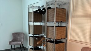 A room with a metal shelving unit holding baskets, two upholstered chairs, and a window with blinds. - Casa Condado Hotel & Residences Rooftop Studio (San Juan)