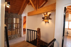 A wooden staircase with a black railing, a stone wall with a mirror, and a rustic wall-mounted light fixture. - 16-PERSON CHALET SKI IN SKI OUT JACUZZI CINEMA ROOM BILLIARDS FOOSBALL (Montgenèvre)