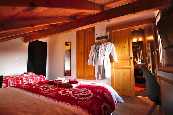A bedroom with a wooden ceiling, a bed with red bedding, a hanging robe, and a mirror on the wall.