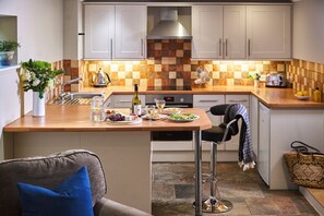 A modern kitchen with a central island, white cabinets, a checkered backsplash, and a dining area with a bar stool.
