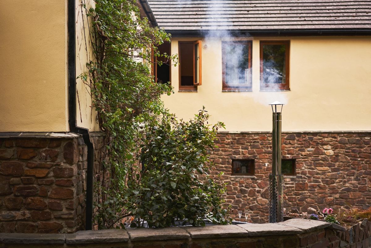 A building with a stone wall, a wooden door, and a chimney emitting smoke.