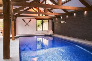 An indoor swimming pool with a wooden ceiling and a stone wall.