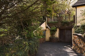 A narrow driveway leading to a wooden gate, surrounded by dense foliage and a stone wall.