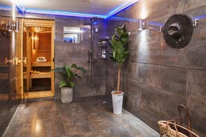 A modern bathroom with a wooden sauna, a large potted plant, and a wall-mounted hat.