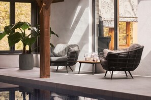 A modern interior with wicker furniture, a potted plant, and a view through large windows.
