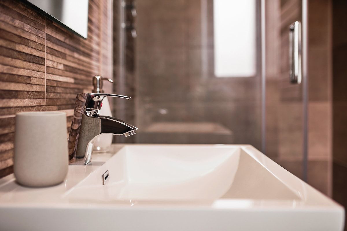 A bathroom with a white sink, a modern faucet, and a glass shower enclosure.