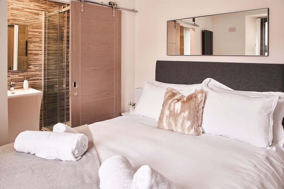 A hotel room with a bed, a bathroom with a shower, a sink, and a mirror.