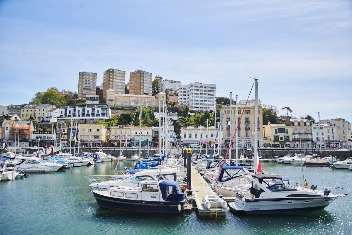 A marina with boats docked, surrounded by buildings with balconies and a clear sky.