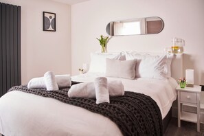 A neatly made bed with towels, a bedside table with a lamp, and a wall-mounted mirror.