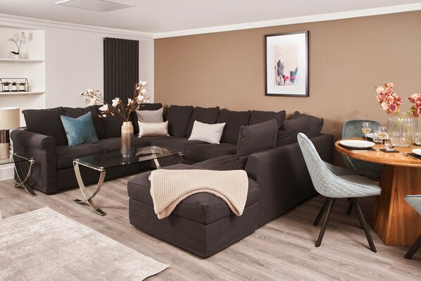 A modern living room with a sectional sofa, a glass coffee table, and a dining area with a wooden table and chairs.