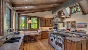 A spacious kitchen with a large island, wooden cabinets, and a stone fireplace. - Fresh Tracks at Northstar- TLUXP (Truckee)