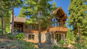 A log cabin with a stone foundation, large windows, and a balcony overlooking a forested area. - Fresh Tracks at Northstar- TLUXP (Truckee)