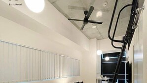 A modern hotel room with a black sofa, a small wooden table, a bed, a ceiling fan, and a TV mounted on the wall. - b hotel Neko Yard | Stylish Loft Studio Central (Hiroshima City)