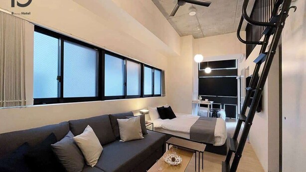 A modern hotel room with a sofa, a bed, a dining area, and a staircase. - b hotel Neko Yard | Stylish Loft Studio Central (Hiroshima City)