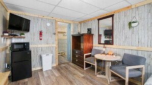Une cuisine compacte équipée d’un réfrigérateur, d’un four à micro-ondes et d’un évier. On y trouve un coin repas avec une table et des chaises, ainsi qu’un petit coin salon avec un canapé.