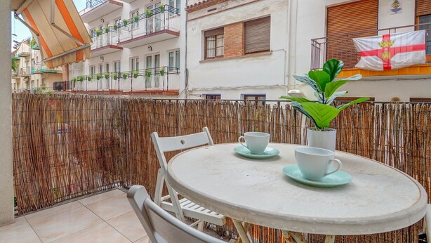 En balkon med et rundt bord, to stole og en potteplante.