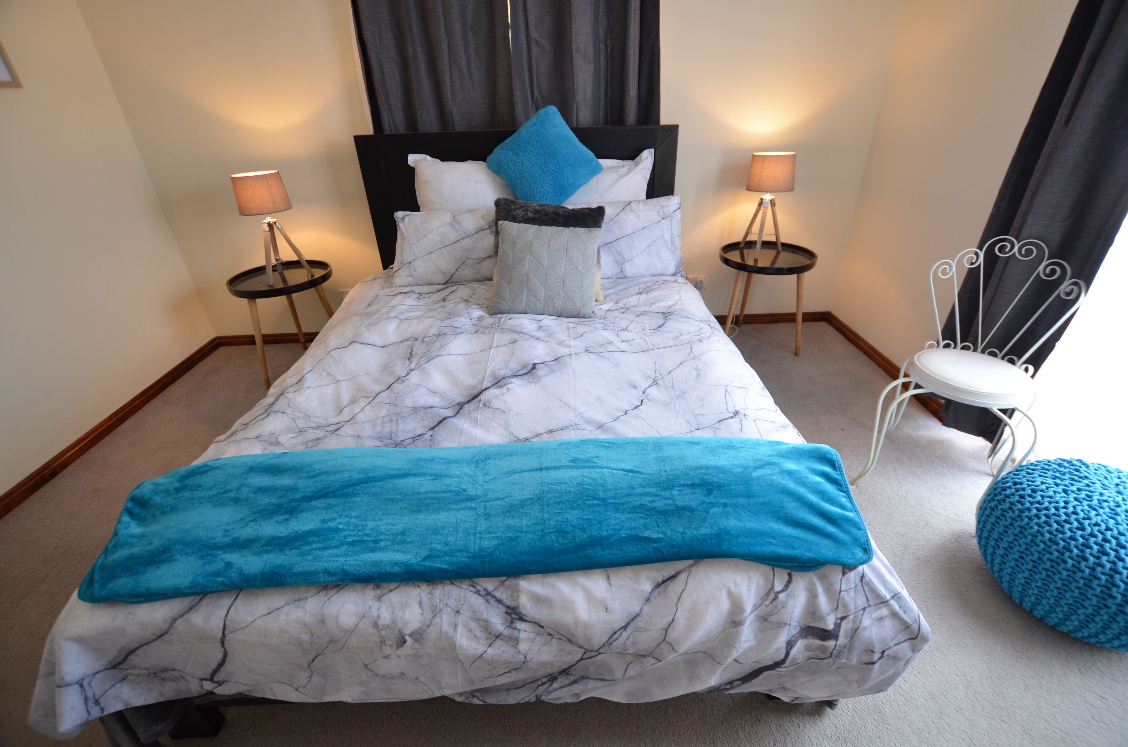 Un lit recouvert d’une couvre-lit à motifs de marbre blanc et bleu, deux lampes de chevet, un oreiller bleu et une chaise blanche avec un coussin bleu.