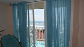 Habitación con vistas al océano a través de un ventanal corredera, una silla de mimbre y piso de baldosas.