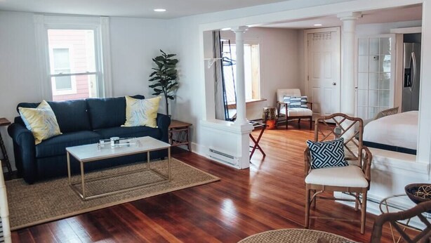 A spacious living room with a dark blue sofa, a coffee table, and a wicker chair. - Modern Chic 1-BR Unit in the Cottages on James (Clayton)