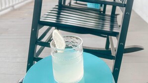 A blue table with a glass of a clear beverage and a lemon slice on a porch with black metal chairs. - Modern Chic 1-BR Unit in the Cottages on James (Clayton)