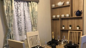 A dining area with a wooden table set for four, chairs, a chandelier, and shelves with tea sets.
