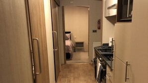 A narrow hallway with wooden flooring leading to a bedroom and a kitchenette.