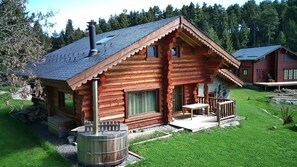 Une cabane rustique en rondins de bois, dotée d’une cheminée, d’un porche et d’une petite terrasse.