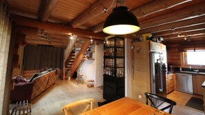Een houten interieur met een eethoek, keuken en een trap naar een hoger niveau.
