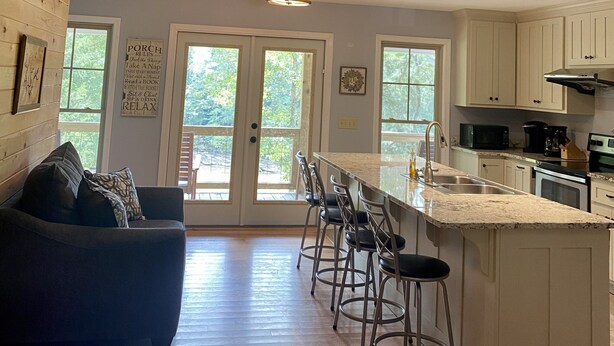 Un vaste espace de vie aménagé dans un style loft, avec un plafond haut, un coin repas doté de tabourets de bar et une cuisine équipée d’appareils électroménagers modernes.