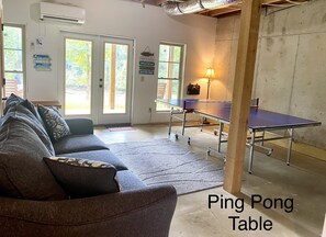 Relax in a spacious room with a ping pong table and comfortable seating area, offering a view of lush greenery.