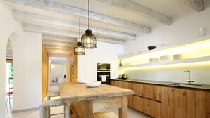 Eine moderne Küche mit Holzschränken, einer Mittelinsel, Pendelleuchten und einem eingebauten Backofen.