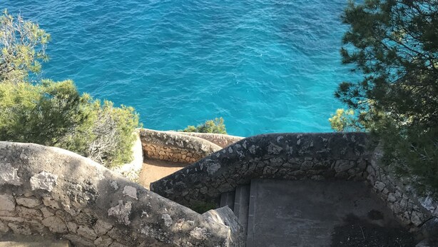 A stone staircase leading down to a coastal area with a view of the sea.