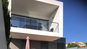 A modern two-story house with a swimming pool, outdoor seating, and a large window overlooking the pool.