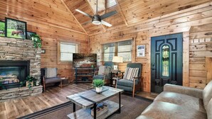 A cozy log cabin interior with a stone fireplace, a ceiling fan, and a comfortable seating area with a sofa and chairs. - Spacious 5 BR/Triple Deck/View from top/close to all attractions in Gatlinburg. (Gatlinburg)
