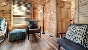 A cozy cabin interior with wooden walls, a wooden floor, a cushioned chair, a bench, and a door. - Spacious 5 BR/Triple Deck/View from top/close to all attractions in Gatlinburg. (Gatlinburg)