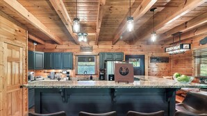 A kitchen with wooden walls, a granite countertop, and a bar area with four chairs. - Spacious 5 BR/Triple Deck/View from top/close to all attractions in Gatlinburg. (Gatlinburg)