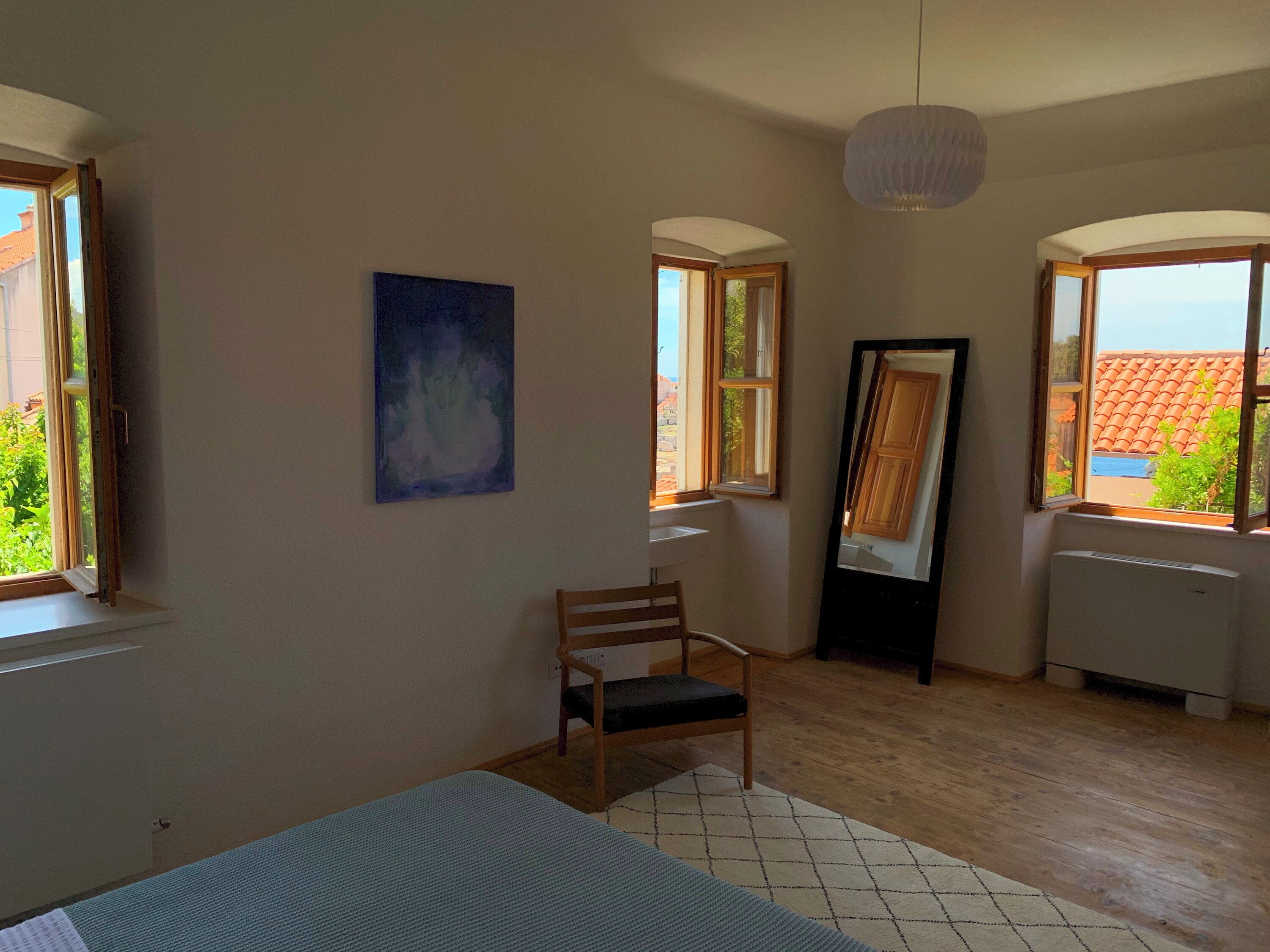 Una stanza con un letto, una sedia, un quadro e una finestra vista edifici.