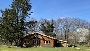 A wooden cabin with a gabled roof, large windows, and a covered porch area. - Maison Type Grange (Andernos les Bains)