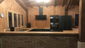 A kitchen with wooden walls, a brick counter, a sink, a stove, and a refrigerator. - Maison Type Grange (Andernos les Bains)