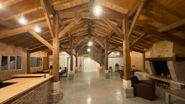 A spacious interior with a high ceiling, wooden beams, a central fireplace, and a bar area. - Maison Type Grange (Andernos les Bains)