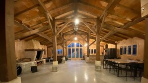 A spacious indoor area with a high ceiling, wooden beams, a central fireplace, and a dining area with chairs and tables. - Maison Type Grange (Andernos les Bains)