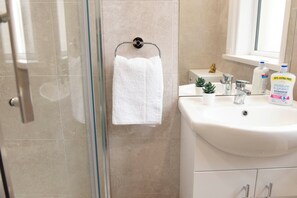 Een badkamer met een douchecabine met glazen deur, een wit wastafelmeubel, een kleine potplant en een fles antibacteriële zeep.