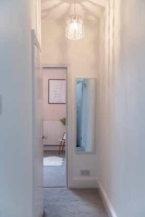 Un corridoio con un lampadario, una citazione motivazionale incorniciata al muro e uno specchio che riflette una porta.