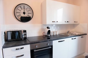 Une cuisine moderne avec des meubles blancs, un plan de travail noir, un four encastré, un four à micro-ondes et une horloge murale.
