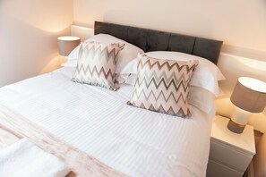 Een net opgemaakt bed met twee gestreepte kussens, een hoofdbord en bedlampjes op een nachtkastje.