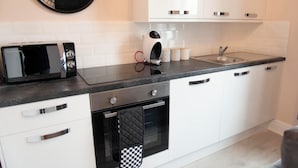 Une cuisine moderne avec des meubles blancs, un plan de travail noir, un four à micro-ondes, une bouilloire et un évier.