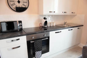 Une cuisine moderne avec des meubles blancs, un plan de travail noir, un four à micro-ondes, une bouilloire et un évier.