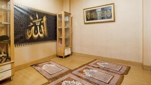A room with a prayer mat, a cabinet, and a framed calligraphy piece on the wall. - OYO 3743 Gania Hotel (Bandung)