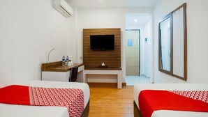 A hotel room with two beds, a TV mounted on a wooden panel, a desk with a chair, and a mirror on the wall. - OYO 3743 Gania Hotel (Bandung)